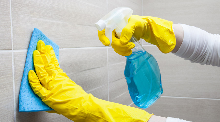person-in-yellow-gloves-cleaning-bathroom-tile-on-wallderry-nh